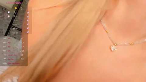 Media: Video of a close-up of a light-skinned woman's bare chest, showing a delicate gold necklace with a small pendant. The background includes blurred text, possibly a calendar or scheduling app.