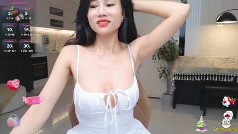 Media: Video of a young Asian woman with long black hair, wearing a white lace dress, sitting in a modern, minimalist kitchen with a sleek white countertop.