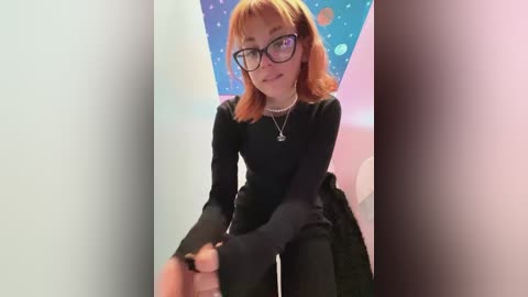 Media: A video of a young woman with short orange hair, wearing black glasses and a black long-sleeved top, seated indoors with a colorful, starry background.