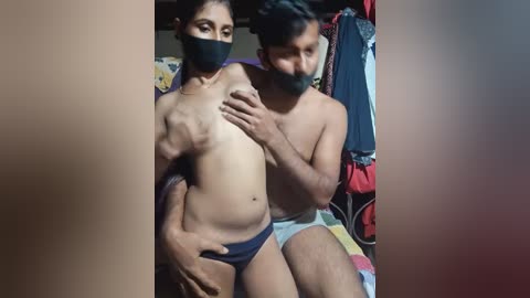 Media: Video of two shirtless South Asian men, one with a black mask, in a cluttered room, partially blurred background.