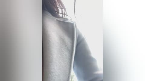 Media: A close-up video of a person's shoulder and arm, wearing a light-colored, textured sweater, against a bright, sunlit background. The image is slightly blurred, emphasizing the soft textures and natural light.