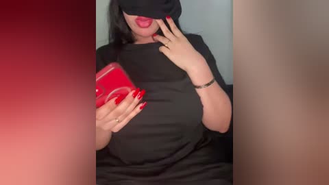 Media: A video of a woman with medium skin tone and dark hair, wearing a black mask, black top, and red nails, holding a red phone.