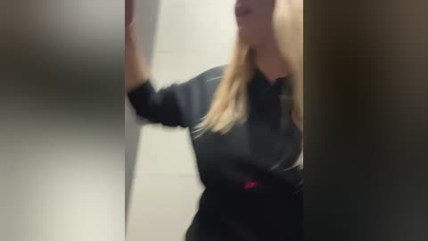 Media: A blurred video shows a blonde woman with fair skin wearing a black leather jacket and standing in a dimly lit, narrow corridor.