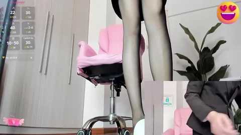 Media: A video shows a woman in a pink chair, wearing black tights, standing on a stool in a modern office with a potted plant and white cabinets.