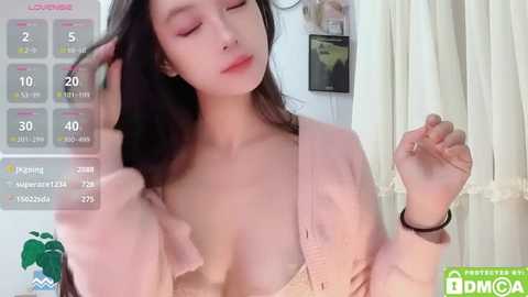 Media: Video of a young Asian woman with long black hair, wearing a pink cardigan, posing indoors with her eyes closed, showing a calendar overlay.