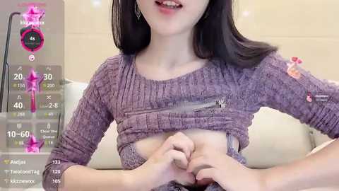 Media: A video of an East Asian woman with straight black hair, wearing a purple knit sweater, lifting her sweater to reveal her flat stomach. The background shows a light-colored wall and a digital interface with various icons.