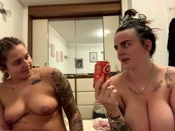 Media: A video of two topless women with tattoos, one holding a can of Coke, standing in a bathroom with white walls and a mirror.