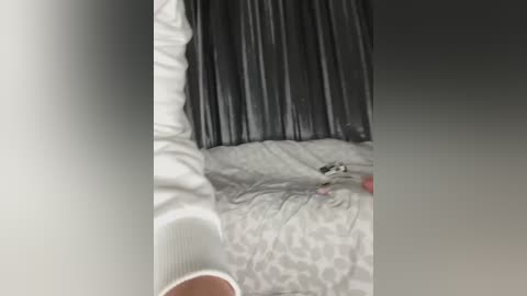 Media: A video showing a person lying on a bed with a black pleated skirt, grey patterned sheets, and white socks visible.