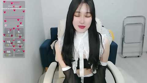 Media: A video of a young East Asian woman with long black hair and fair skin in a revealing black and white maid outfit, sitting in a chair, with a chart of heart emojis in the background.