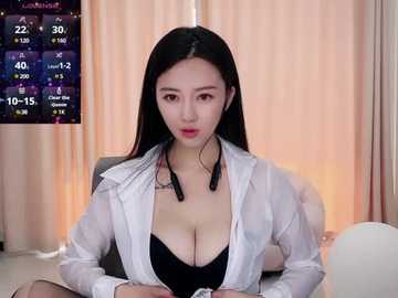 Media: A video of a young East Asian woman with long black hair, wearing a semi-transparent white blouse revealing a black bra, sitting in a room with beige curtains.