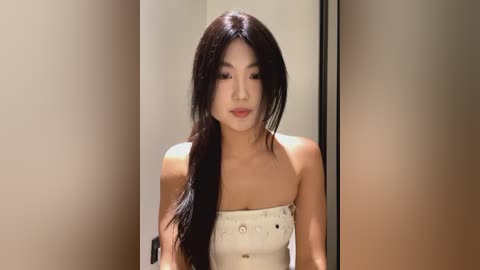 Media: Video of a young Asian woman with long, straight black hair, wearing a strapless white dress, standing in front of beige walls.