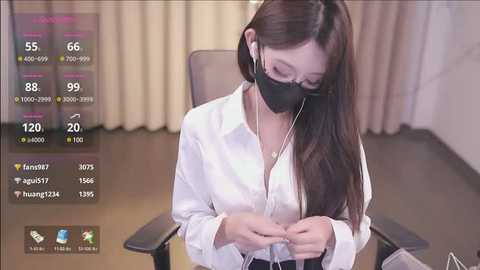 Media: A video of an Asian woman in a white blouse and black mask, wearing headphones, sitting at a desk in a dimly lit room with beige curtains.