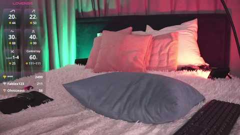 Media: Video of a cozy bedroom with a plush white bed, pink and white pillows, and a large, light blue pillow. The room is softly lit with green and pink ambient lighting.