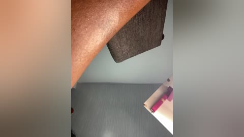 Media: A video showing a close-up of a dark-skinned arm with raised, textured skin, and a grey wall with a grey sofa.