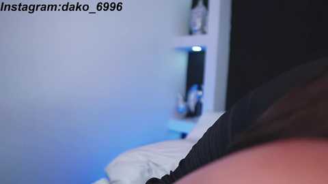 Media: Video of a dimly-lit bedroom with a bed featuring white sheets and a dark pillow. The wall behind the bed displays a digital clock and a small decorative item. The image includes a watermark \"instagram/dako_6999\" in the top left corner.