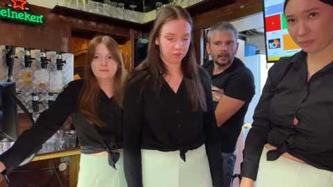 Media: Video of two young women in black shirts and white skirts, flanked by two men in casual attire, inside a dimly lit bar with neon signs and shelves of alcohol.