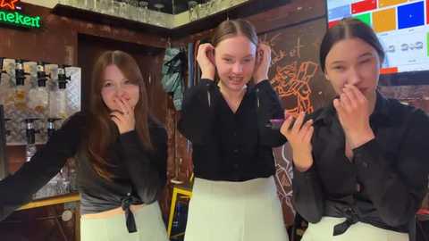 Media: Video of three young women in a cozy bar; one with long brown hair tied in a knot, another with long brown hair in ponytail, and the third with long brown hair in a bun, all smiling.