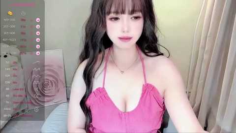 Media: Video of an Asian woman with long black hair, wearing a pink halter top, sitting indoors.