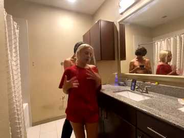 Media: A video of a blonde woman in a red outfit and black hairband taking a selfie in a modern bathroom with beige walls, a granite countertop, and a large mirror.