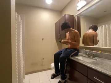 Media: Video of a shirtless man in a bathroom, sitting on a countertop, texting, with a mirror reflecting his back.