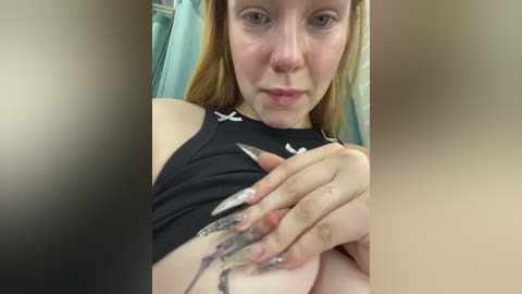 Media: Video of a fair-skinned woman with long blonde hair, wearing a black Under Armour sports top, lifting her shirt to reveal a tattoo of a snake on her ribcage.