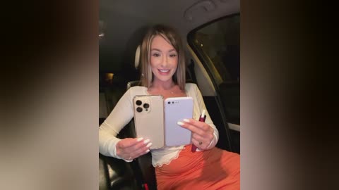 Media: Video of a smiling, fair-skinned woman with long blonde hair in a white top and orange skirt, taking a selfie in a car.