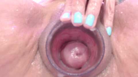 Media: A close-up video of a vagina, showing the pink, moist inner walls with a hand with turquoise-painted nails gently spreading the labia. The background is blurred, focusing attention on the intimate details.