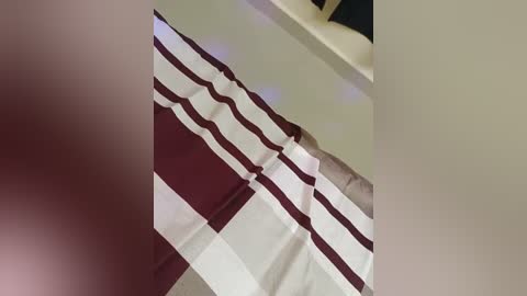 Media: A video of a beige bathroom floor with a maroon and white checkered bath mat placed diagonally, partially covering a white bathtub. The image is slightly blurred and the lighting is soft.