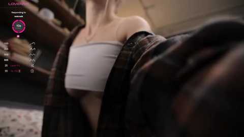 Media: Video of a woman in a white off-the-shoulder crop top, partially unbuttoned plaid shirt, blurry background.