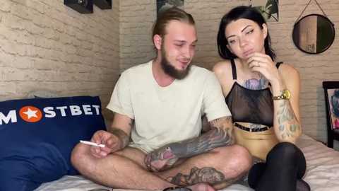 Media: A video shows a tattooed man and a woman in lingerie sitting on a bed, smoking, with a brick wall backdrop and a \"Mostbet\" pillow.