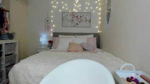 Media: Video of a cozy, pastel-themed bedroom with white walls, a plush white bed, soft pink pillows, fairy lights, dreamcatcher, and a white bathtub in the foreground.