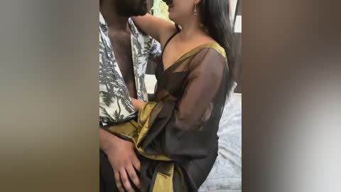 Media: Video of a dark-skinned man in a floral shirt, holding a South Asian woman with long black hair and a black, yellow saree, in a close embrace.