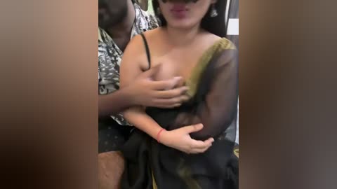 Media: Video of an Asian woman with medium-sized breasts, wearing a sheer black blouse, being fondled by a man with a dark complexion, partially obscured by the frame.