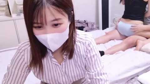 Media: Video of an Asian woman in a striped shirt and face mask, lying on a bed, being massaged by another woman in a black top and light blue underwear.