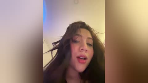 Media: A blurry video of a young woman with long, dark hair, light skin, and slightly open mouth, taken in a dimly lit room with a soft blue hue.