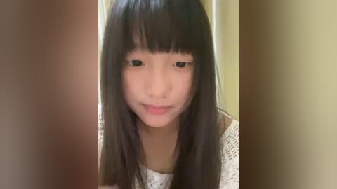 Media: Video of an East Asian girl with long, straight black hair, wearing a white, crocheted sweater, standing against a beige and brown background. She has a neutral expression.