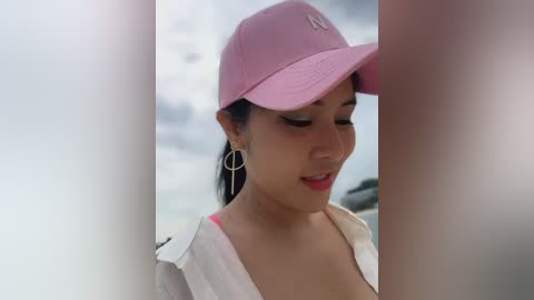 Media: A video of a young Asian woman with light skin, wearing a pink baseball cap and white shirt, smiling, with a blurred background.