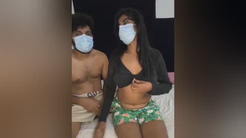 Media: Video of two South Asian individuals wearing face masks, one topless with a belt, the other in a crop top and floral shorts.