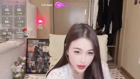 Media: A video of an Asian woman with fair skin, long black hair, and red lipstick, sitting in a cozy bedroom with a framed collage, a window, and a wardrobe.