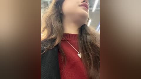 Media: Video of a young woman with fair skin, brown wavy hair, wearing a red sweater and black cardigan, seen from the neck up, with a blurred background.