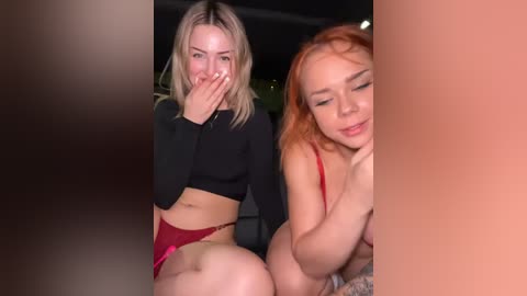 Media: Video of two young women in a dimly-lit room: one blonde with a black crop top, red panties, covering her mouth; the other redhead in a red bra, smiling.