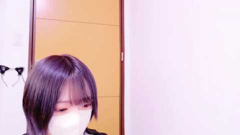 Media: A video of a person with short, dark hair and a white mask, partially visible against a light-colored wall with a door.