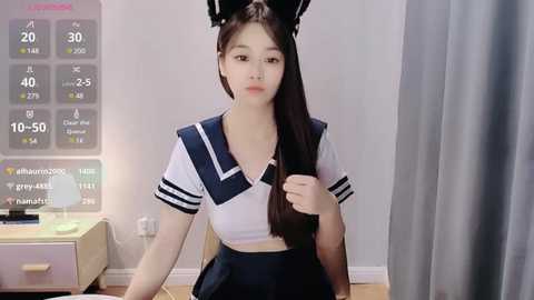 Media: Video of an East Asian woman with long black hair, wearing a sailor schoolgirl outfit, seated in a modern room with a digital display showing fitness stats.