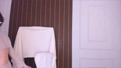 Media: A video of a modern bathroom with a white towel hanging on a brown, vertically striped wall, next to a white door with a subtle pattern.