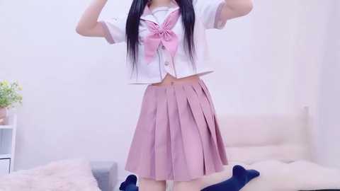 Media: Video of an Asian woman with long black hair, wearing a pink sailor school uniform and a white cropped top, posing indoors.