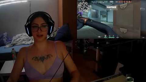 Media: Video of a woman with glasses and black headphones, wearing a lavender bra, in a dimly lit room, playing a video game on a monitor.