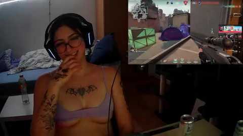 Media: Video of a tattooed woman in a purple bra, wearing headphones, smiling, in a dimly lit bedroom. Inset: video game screen of a car racing game.