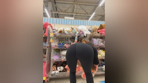 Media: Video of a woman bending over in a toy store, wearing tight black leggings, with plush toys on shelves in the background.