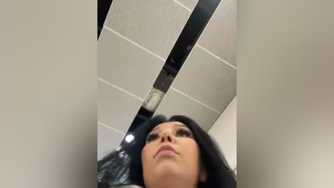 Media: A low-angle video of a woman with long black hair, looking up at a ceiling with a large crack running diagonally. The ceiling tiles are white with a light gray pattern.