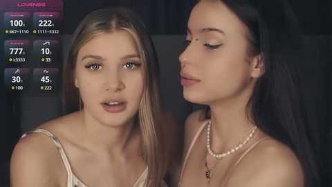 Media: Video of two young women, one blonde and one brunette, in a dimly lit room, wearing casual outfits. They appear close, with the blonde woman looking concerned and the brunette with a serene expression.